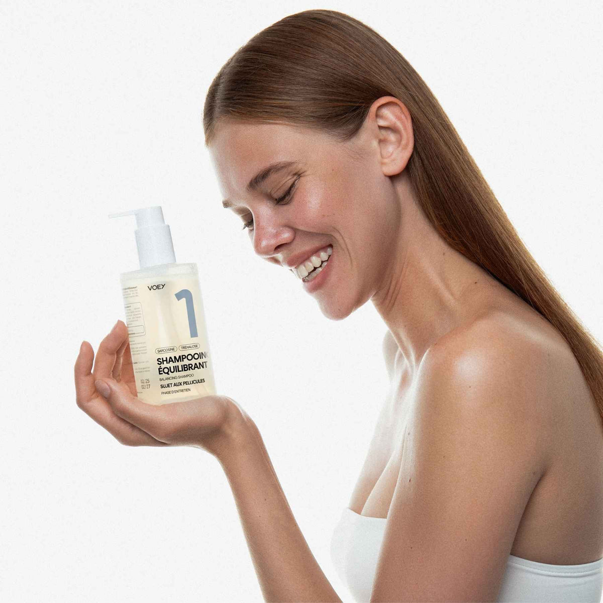 Woman holding a bottle of shampoo with a plain background