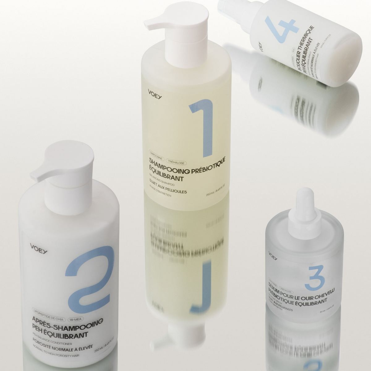 Four white shampoo and conditioner bottles from Voey, arranged on a glossy white reflective surface. The center bottle is a large pump bottle labeled '1', flanked by a smaller pump bottle labeled '2' on the left, a smaller dropper bottle labeled '3' on the right, and another pump bottle labeled '4' in the upper right.