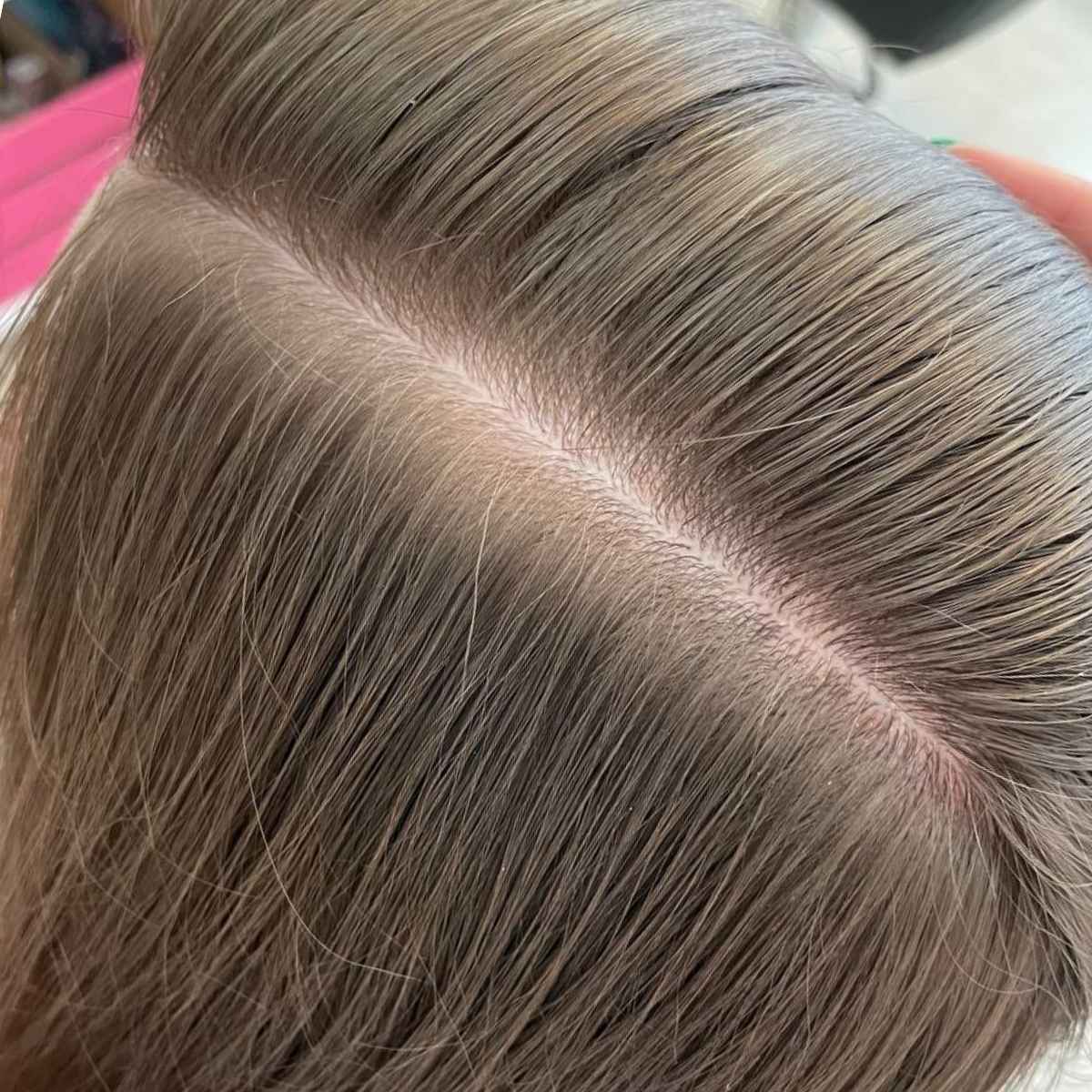 Close-up of a person's hair with a clean center part, showing light brown to ash brown hair texture and color.