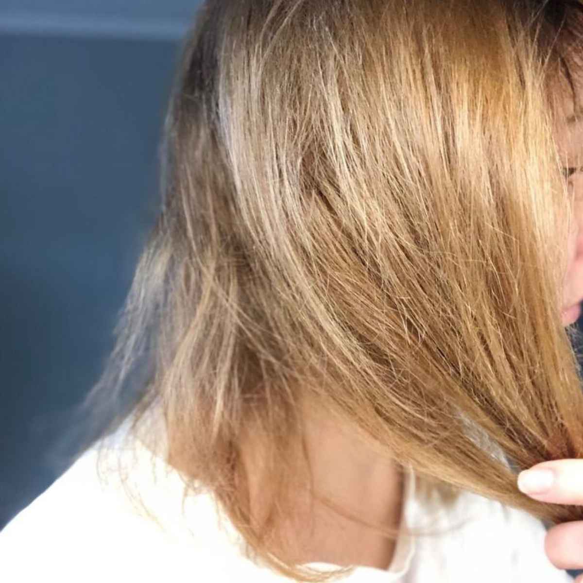Close-up of a person's shoulder-length blonde hair, showing the texture and color of the hair being held by a hand.