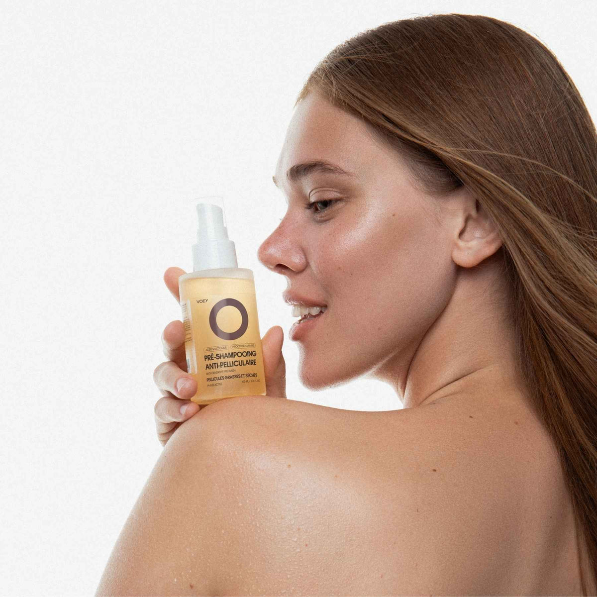 Woman holding a bottle of skincare product with a plain background
