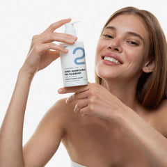 A smiling woman holds up a white bottle of 2OT Hair-Shampooing-PH-Equilibrant hair shampoo against a clean white background.
