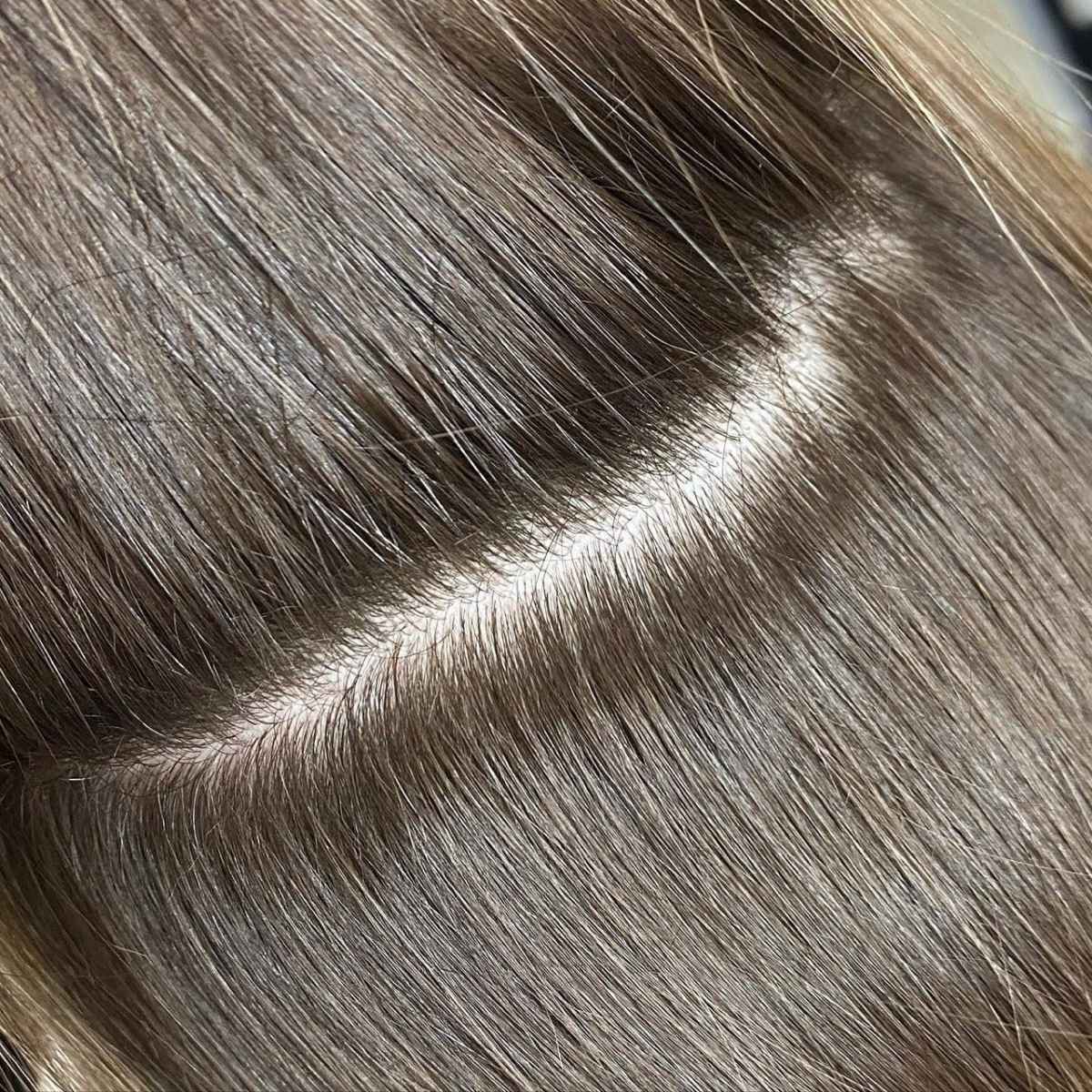 Close-up of smooth, straight hair with a light brown to ash blonde color and a visible part line.