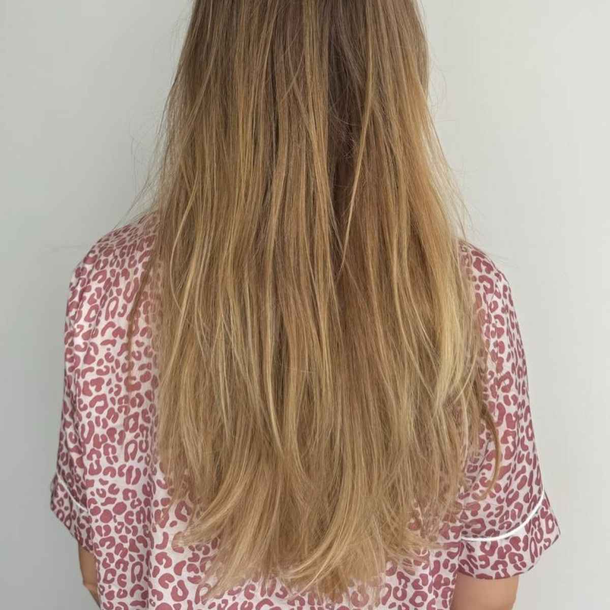 Long, straight blonde hair shown from the back of a person wearing a pink and white leopard print top against a plain light gray background.